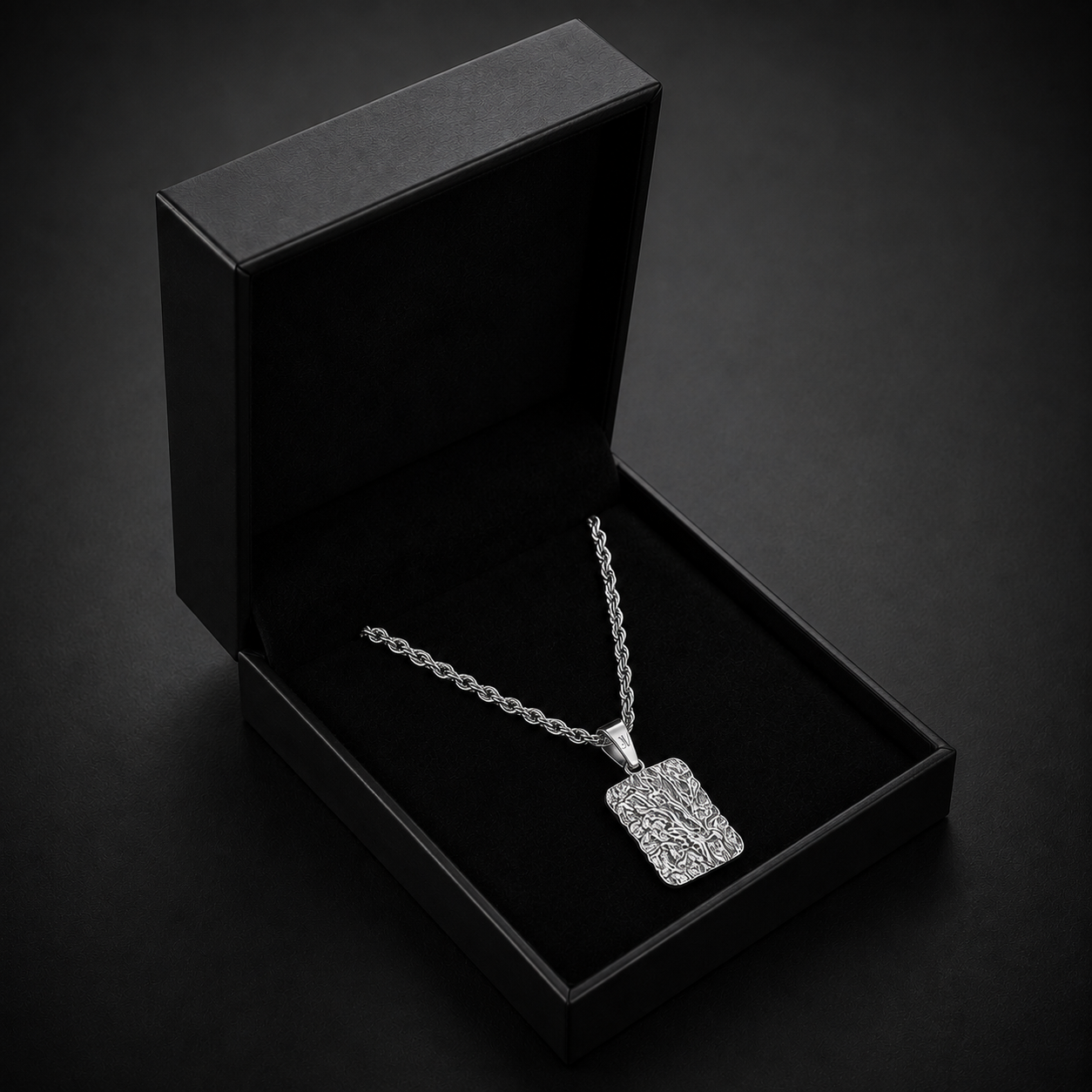 Zilverkleurige getextureerde lava-taghanger aan een koordketting van 3mm in een open zwart JVillion cadeaudoosje