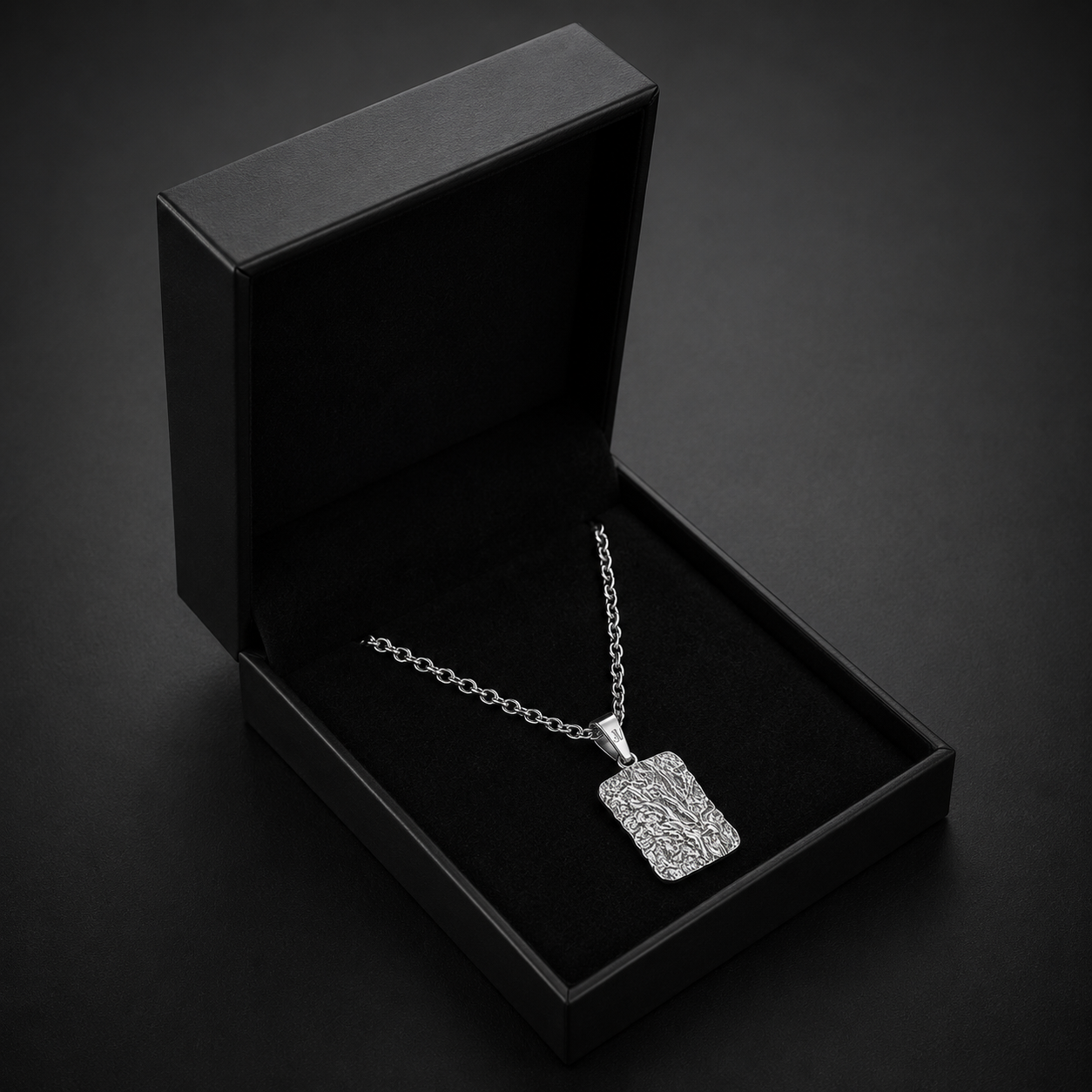Zilverkleurige getextureerde lava-taghanger aan een jasseronketting in een zwart JVillion cadeaudoosje