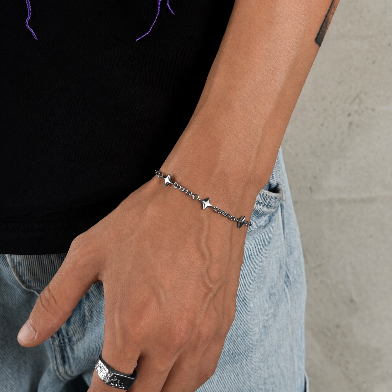 Pulseira de elos estrela prateada usada no pulso com t-shirt preta e calças de ganga, JVillion